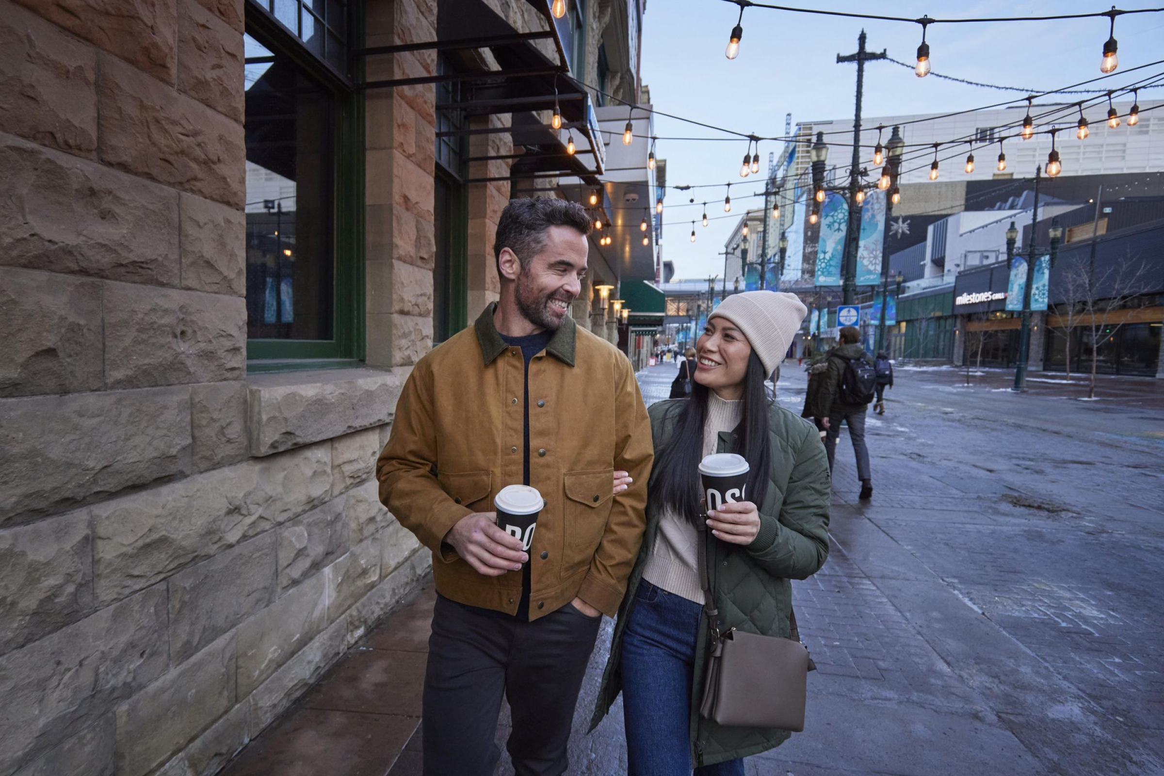 A couple walking down Stephen Ave holding coffee.